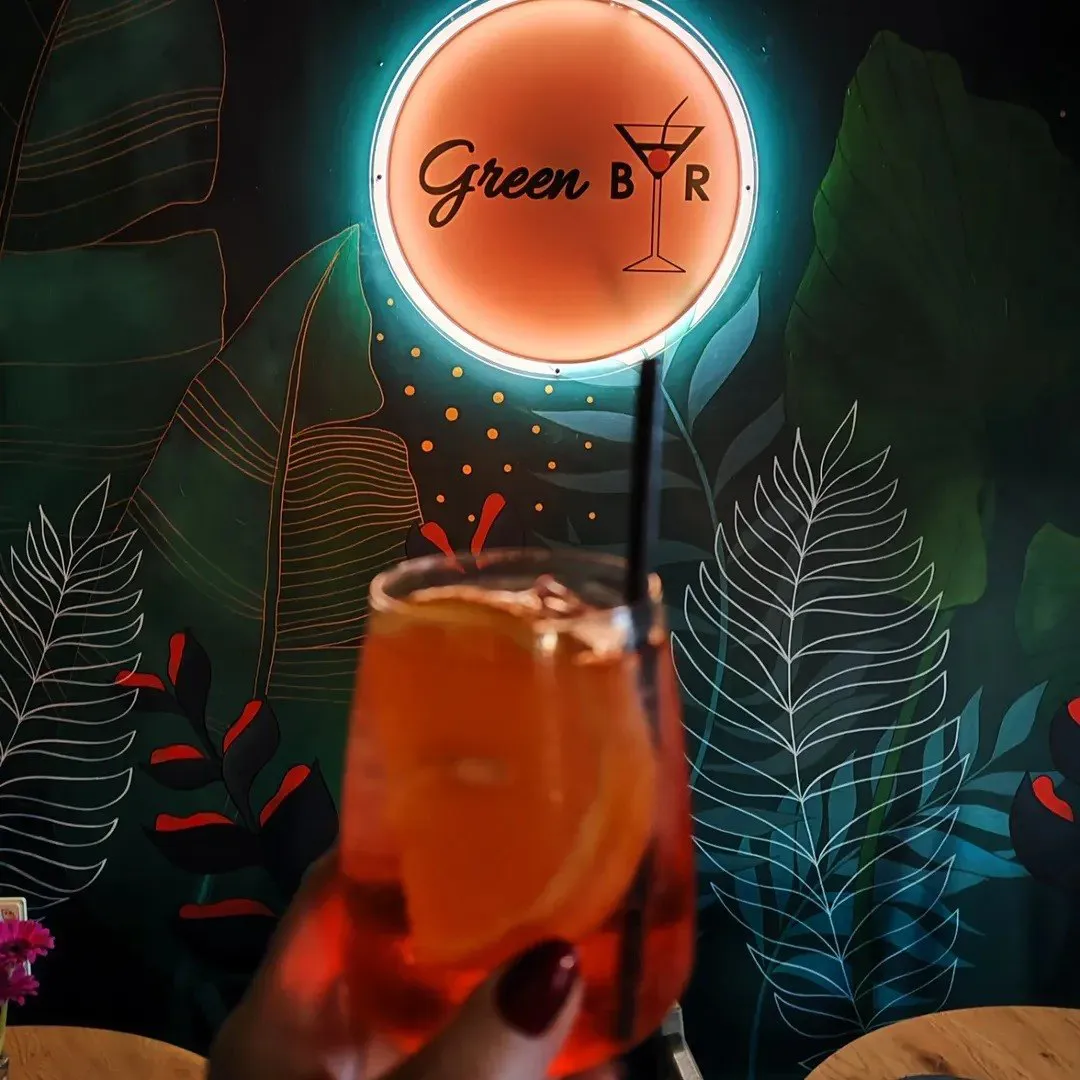 Oranžs kokteilis pacelts pret Green Bar neona zīmi